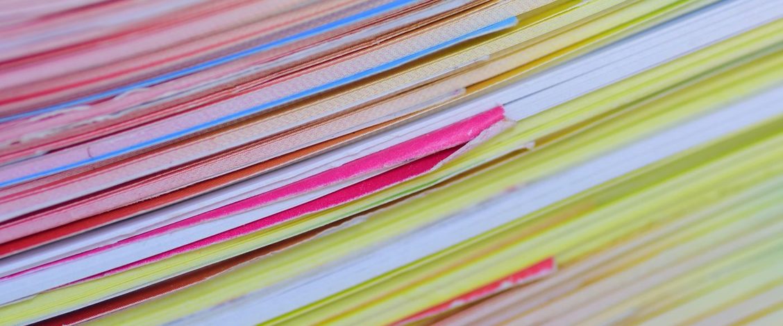The edges of a tall stack of coloured papers and folders in pink, yellow, blue and white, seen close up and side on