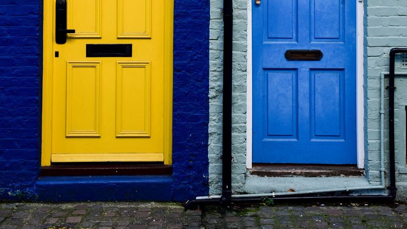 A yellow front door and a blue front door side by side in a London terrace, set in walls of dark blue and pale green brick